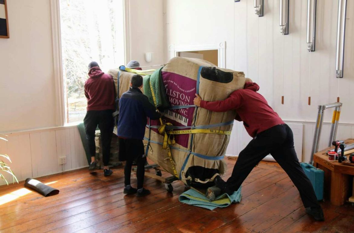 Des déménageurs professionnels transportent avec précaution un piano emballé dans un salon, illustrant quelle assurance couvre les dégâts pendant un déménagement.