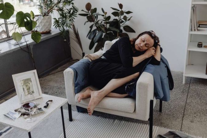 Une femme en robe noire se repose paisiblement dans un fauteuil confortable, illustrant l'aspect reposant que l'on recherche lors d'une expérience de couchsurfing.