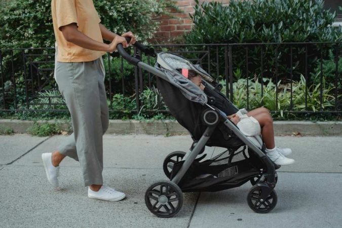 Une femme promène son enfant dans une poussette citadine sur un trottoir, essentielle pour bien choisir la poussette idéale.