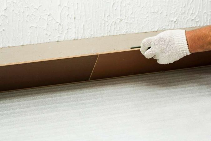 Un ouvrier pose des baguettes de finition le long d'un mur blanc.
