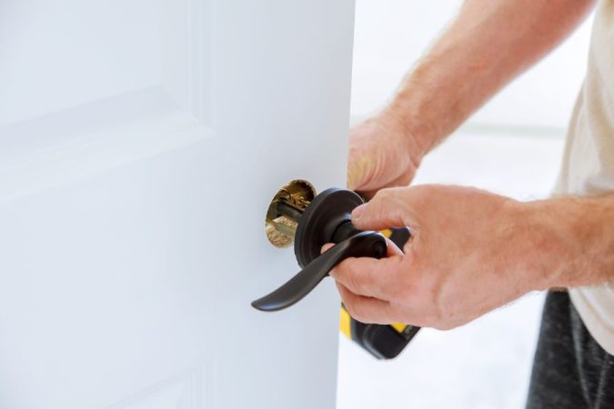 Gros plan sur les mains d'un bricoleur manipulant un mécanisme sombre pour installer une poignée blindée porte.   